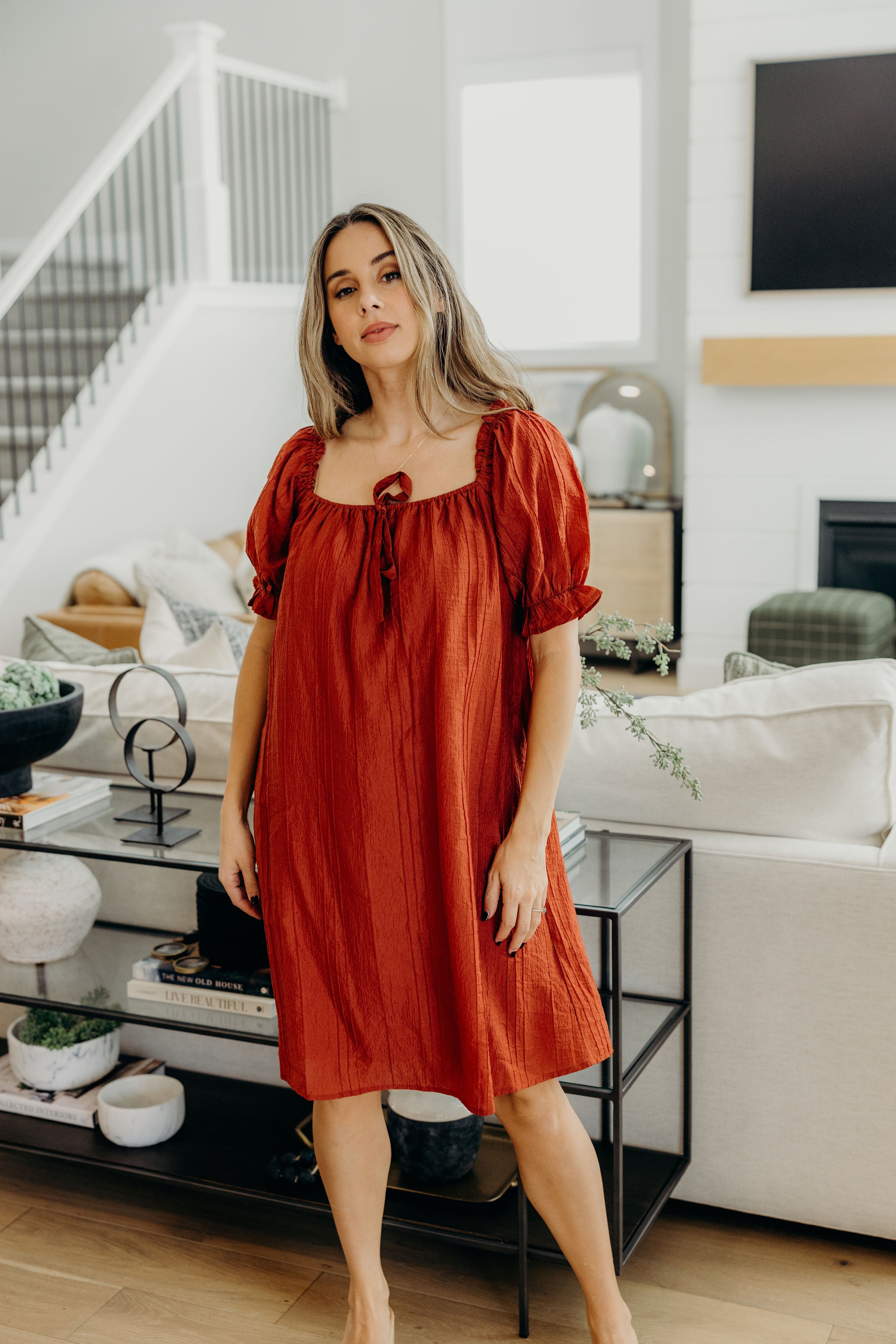 Brick red knee length shift dress with square neckline, and half length puff sleeves with ruffle and tie detail.